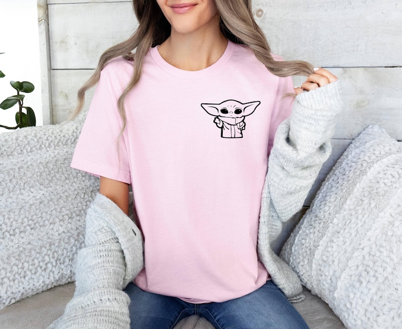 May include: A pink t-shirt with a black and white illustration of a character from the Star Wars franchise, The Mandalorian, known as "The Child" or "Baby Yoda".