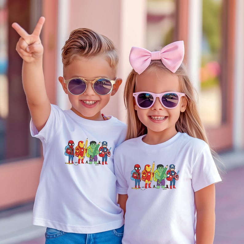 May include: Two children wearing white t-shirts with a colorful graphic of superheroes. The boy is wearing sunglasses and giving a peace sign. The girl is wearing a pink bow and sunglasses. The shirts feature Spider-Man, Iron Man, Hulk, and Captain America.
