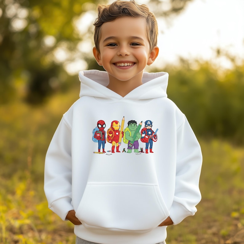 May include: A white hooded sweatshirt featuring a colorful graphic of cartoon superheroes, including Spider-Man, Iron Man, Hulk, and Captain America, each holding school supplies. The design is centered on the front of the sweatshirt.