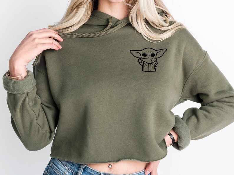 May include: A green cropped hoodie with a black graphic of a cartoon character on the front. The character is a small, green creature with large ears and a mischievous expression.