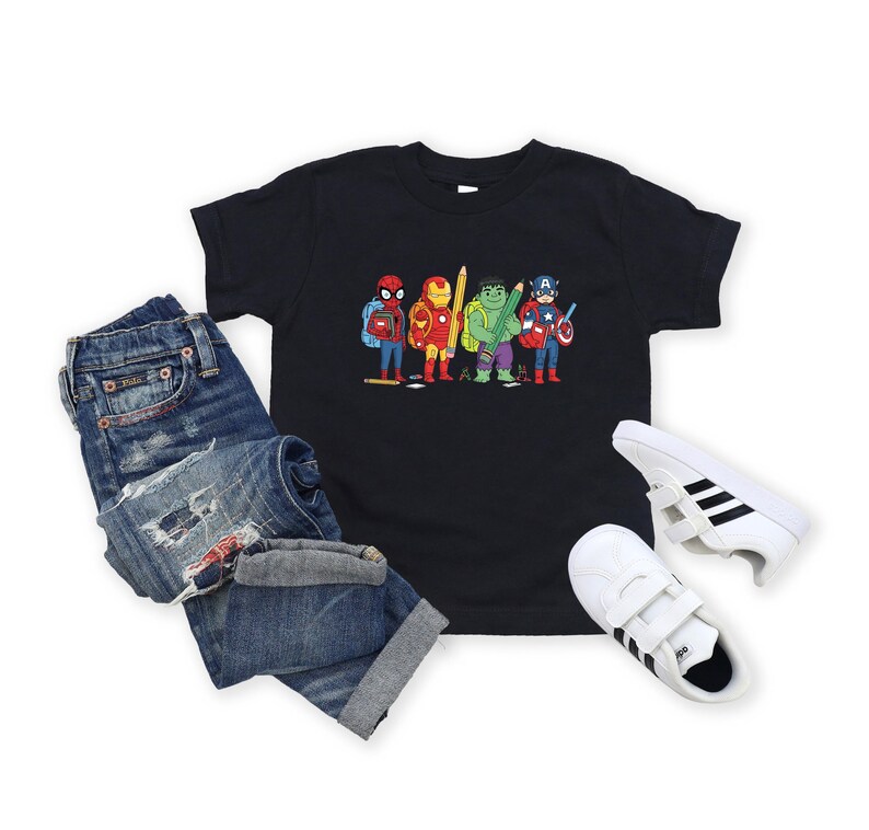 May include: A black t-shirt featuring a cartoon illustration of several superheroes, including Spider-Man, Iron Man, Hulk, and Captain America. The shirt is paired with blue denim jeans and white sneakers with black stripes.