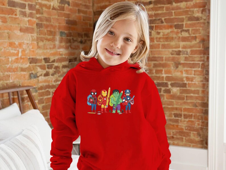 May include: A red hooded sweatshirt featuring a colorful graphic of several superheroes, including Spider-Man, Iron Man, Hulk, and Captain America. The sweatshirt is worn by a young person with blonde hair.