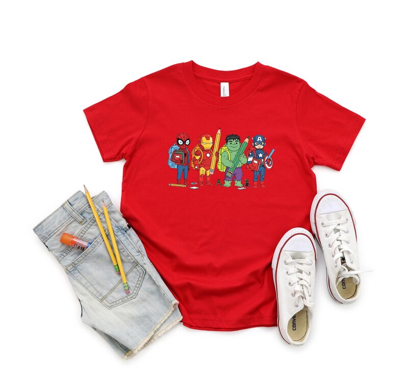 May include: A red t-shirt featuring a cartoon illustration of superheroes, including Spider-Man, Iron Man, Hulk, and Captain America, each holding school supplies. The shirt is paired with denim shorts, pencils, glue stick, and white sneakers.