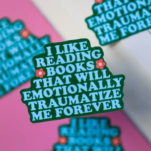 May include: Three stickers with a green background and blue text that reads "I like reading books that will emotionally traumatize me forever". Each sticker has a small pink flower graphic.