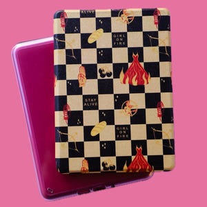 May include: A black and gold checkered e-reader case with a design featuring the words "Girl on Fire" and "Stay Alive".