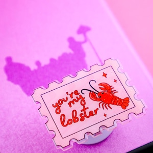 May include: A pink phone case with a clear phone grip featuring a red lobster with the text "you're my lobster" in white.