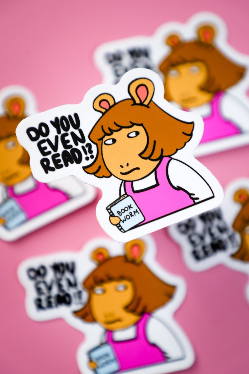 May include: A sticker featuring a cartoon character with brown hair and ears, wearing a pink dress. The sticker has the text "DO YOU EVEN READ?!" and the character is holding a book labeled "BOOK WORM". The background is pink.