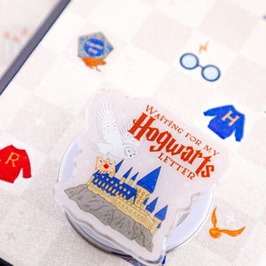 May include: A white phone case with a clear plastic sticker featuring a white owl flying over Hogwarts castle. The sticker says "Waiting for my Hogwarts Letter".