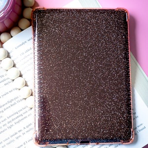 May include: A close-up of a rose gold glitter phone case. The case is made of a hard plastic material and has a smooth, shiny finish. The glitter is evenly distributed throughout the case, giving it a sparkly appearance.