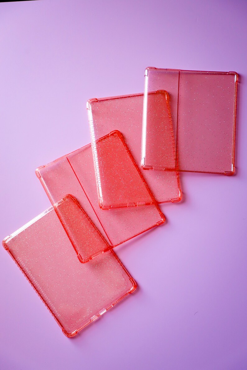May include: Five pink glitter phone cases stacked on top of each other on a light purple background.