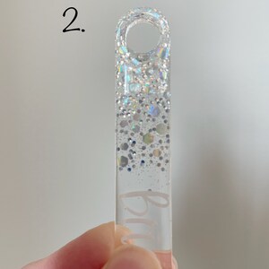 K&ouml;nnte beinhalten: Ein durchsichtiger Acryl-Schl&uuml;sselanh&auml;nger mit silbernem Glitzer-Design und dem Wort "Blau" auf der Vorderseite.