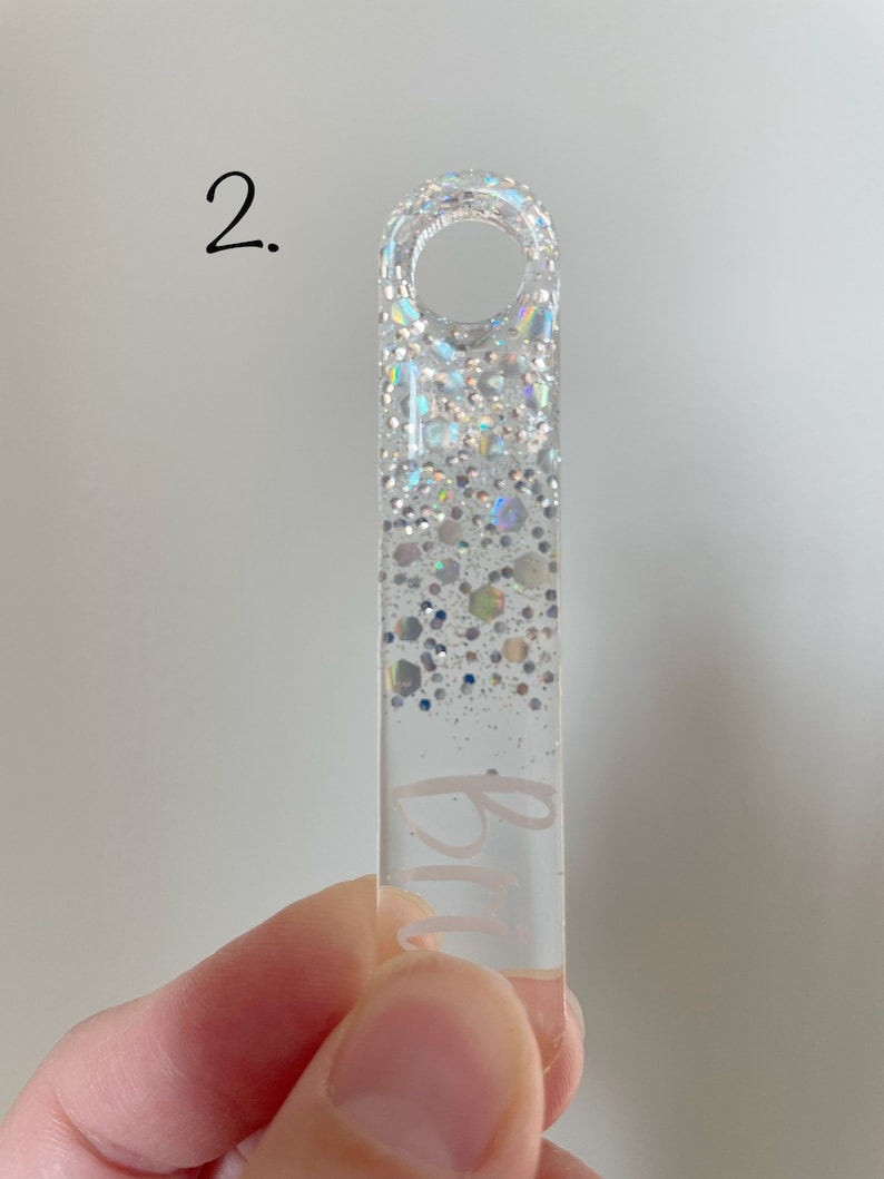 K&ouml;nnte beinhalten: Ein durchsichtiger Acryl-Schl&uuml;sselanh&auml;nger mit silbernem Glitzer-Design und dem Wort "Blau" auf der Vorderseite.