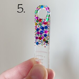 K&ouml;nnte beinhalten: Ein durchsichtiger Acryl-Schl&uuml;sselanh&auml;nger mit einem Regenbogen-Glitzer-Design und dem Wort "Lily" darauf.