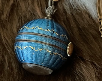 May include: A blue and gold enameled spherical pendant with a clear bottom. The pendant is suspended from a gold-colored chain and clasp. The blue enamel is decorated with gold filigree and a textured pattern.