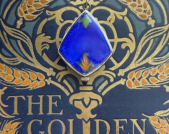 May include: A silver pendant with a blue, diamond-shaped enamel design, accented with green and orange details. The pendant hangs over a book cover with gold lettering that reads "THE GOLDEN KEY" by Henry Van Dyke.