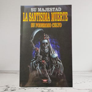 May include: A book titled "SU MAJESTAD LA SANTISIMA MUERTE SU PODEROSO CULTO" features a skeletal figure with a crown, holding a scythe and a scale. The cover is predominantly black with gold and red lettering and a blue background.