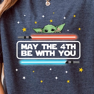 K&ouml;nnte beinhalten: Ein heidefarbenes marineblaues T-Shirt mit einem Aufdruck eines gr&uuml;nen Au&szlig;erirdischen mit dem Text "May the 4th Be With You".