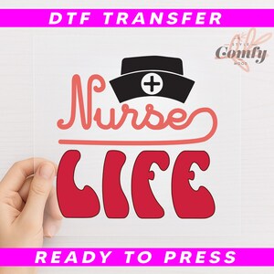 May include: A clear DTF transfer sheet with the words "Nurse Life" in red and a black nurse's cap with a white cross. The words "DTF TRANSFER" and "READY TO PRESS" are in pink.