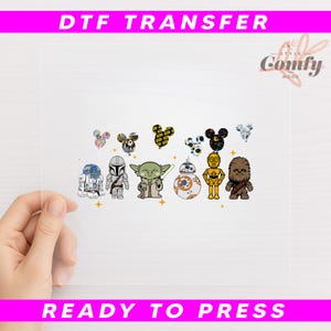 May include: A clear DTF transfer sheet featuring cartoon characters from Star Wars and Mickey Mouse. The characters include R2-D2, a Mandalorian, Yoda, BB-8, C-3PO, and Chewbacca. The sheet also has the text "DTF TRANSFER" and "READY TO PRESS".