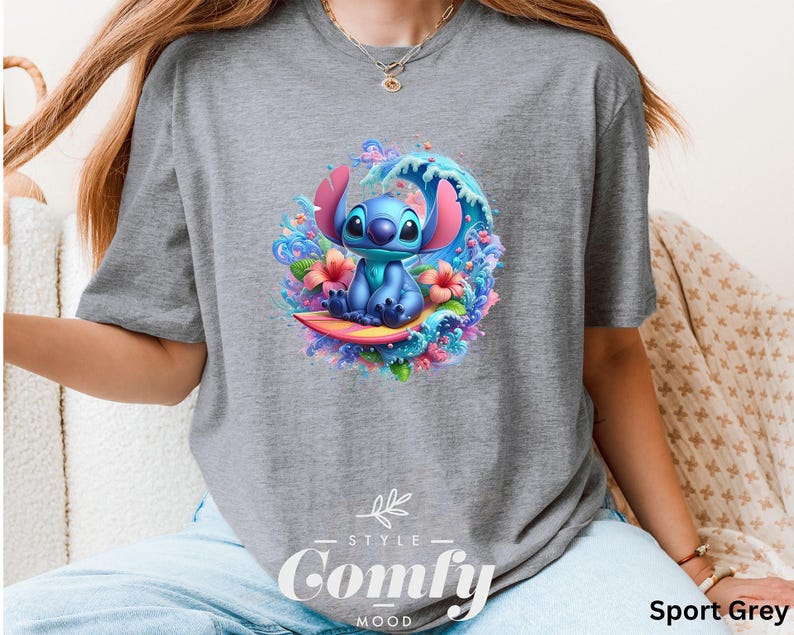 Może przedstawiać: Szara koszulka sportowa z kolorową grafiką postaci Stitch z filmu Lilo & Stitch. Stitch jest przedstawiony na ż&oacute;łtej desce surfingowej, otoczony falą i kwiatami. Koszulka ma napis "Style Comfy Mood".