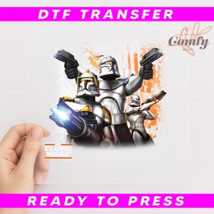 May include: DTF transfer featuring a graphic of Clone Troopers from Clone Wars. The image shows three troopers in silver and white armor, holding blasters. The text "DTF TRANSFER" and "READY TO PRESS" are displayed in pink.