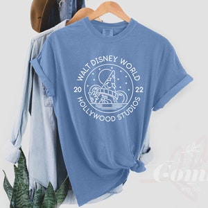 Puede incluir: Una camiseta azul claro con un dise&ntilde;o gr&aacute;fico blanco de un castillo y el texto "Walt Disney World 20 Hollywood Studios 22".