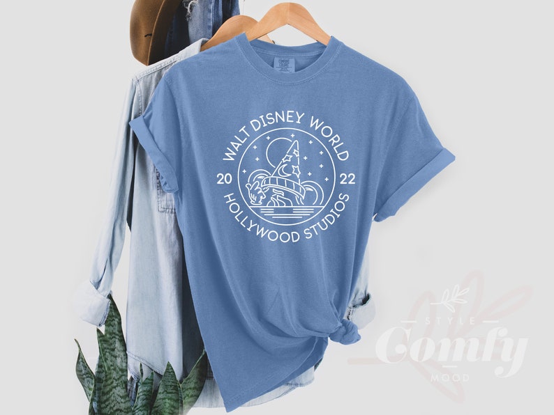 Puede incluir: Una camiseta azul claro con un dise&ntilde;o gr&aacute;fico blanco de un castillo y el texto "Walt Disney World 20 Hollywood Studios 22".