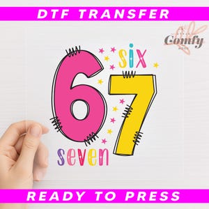 May include: A DTF transfer with a large pink number 6 and a yellow number 7, outlined in black. The word "six" is above the 7, and "seven" is below. The text "DTF TRANSFER" and "READY TO PRESS" are in pink.