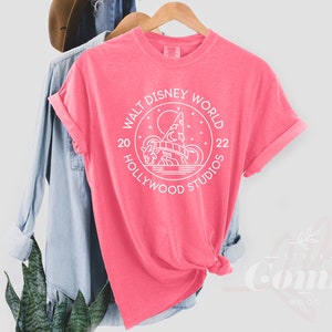 Puede incluir: Camiseta rosa con un gr&aacute;fico blanco del logotipo de Walt Disney World Hollywood Studios. El logotipo presenta una imagen estilizada de las colinas de Hollywood y el texto "Walt Disney World 20 Hollywood Studios 22".