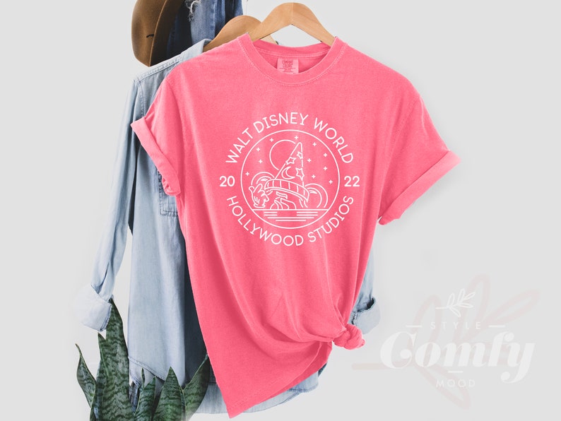 Puede incluir: Camiseta rosa con un gr&aacute;fico blanco del logotipo de Walt Disney World Hollywood Studios. El logotipo presenta una imagen estilizada de las colinas de Hollywood y el texto "Walt Disney World 20 Hollywood Studios 22".