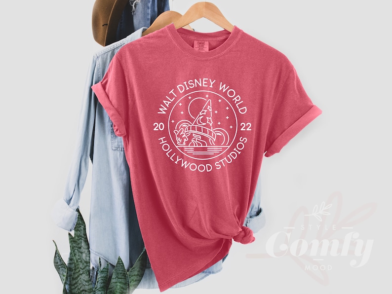 Puede incluir: Una camiseta roja con un dise&ntilde;o gr&aacute;fico blanco en forma de c&iacute;rculo con el texto "Walt Disney World 20 Hollywood Studios 22" y una imagen estilizada del Hollywood Tower Hotel.