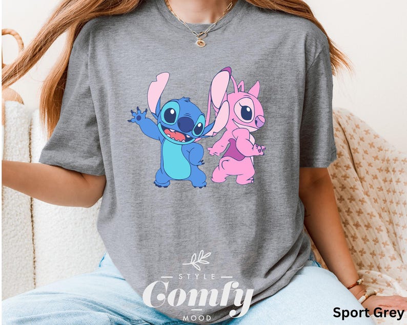 May include: Sport grey t-shirt featuring a cartoon graphic of Stitch and Angel. Stitch is blue with large ears, and Angel is pink. The shirt has the words "STYLE" and "Comfy MOOD" printed on it.
