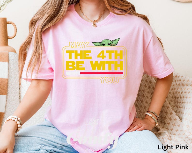 May include: A light pink t-shirt with a graphic of a green alien peeking out of a box with the text "May the 4th be with you".