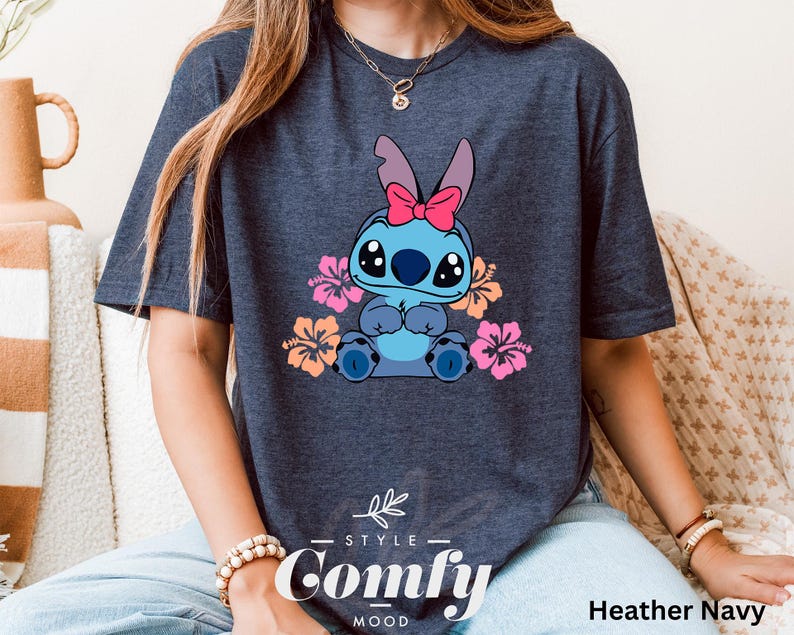 May include: A heather navy blue t-shirt featuring a cartoon Stitch character with pink flowers. The shirt has the text "Comfy" printed on the bottom.