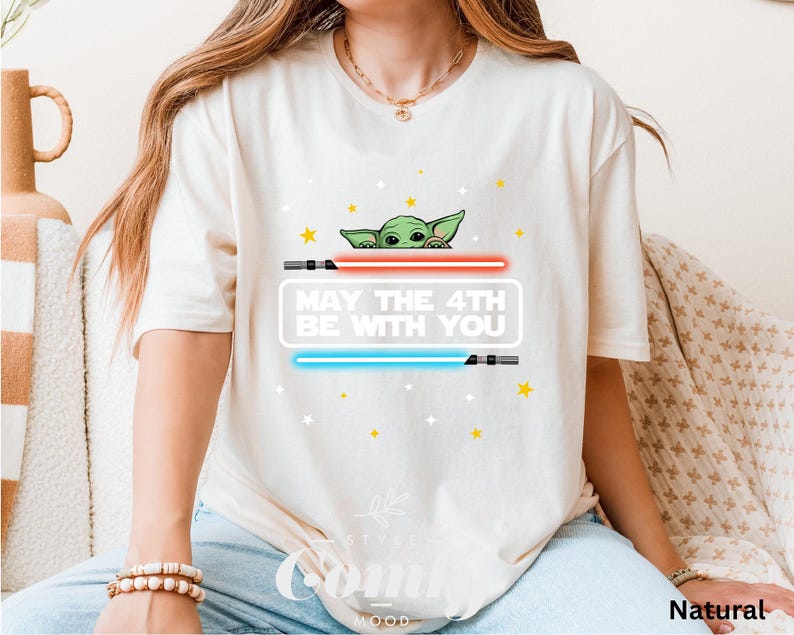 K&ouml;nnte beinhalten: Wei&szlig;es T-Shirt mit einem gr&uuml;nen Alien-Charakter, der hinter einem Lichtschwert hervorlugt. Der Text "May the 4th Be With You" ist auf das Shirt gedruckt.