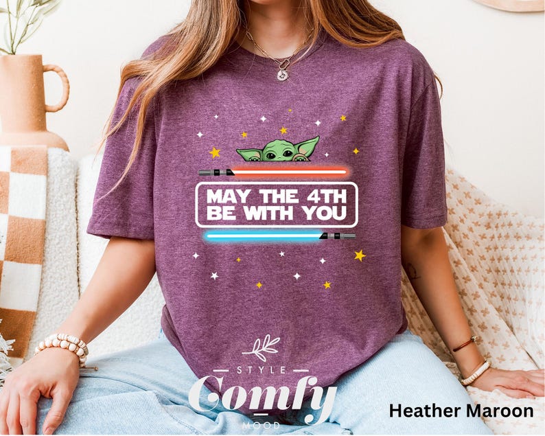 K&ouml;nnte beinhalten: Ein T-Shirt in Heide-Maroon mit einem Motiv eines gr&uuml;nen Au&szlig;erirdischen, der hinter einem Lichtschwert hervorlugt. Der Text "May the 4th Be With You" ist auf dem T-Shirt aufgedruckt.