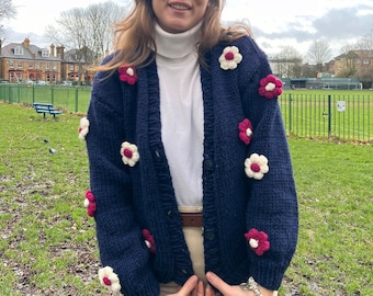 May include: A navy blue cardigan with white and pink crocheted flowers. The cardigan has a button closure and is made of a soft, knitted fabric.