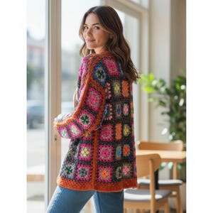 May include: A colorful, crocheted cardigan with a floral pattern. The sweater features a patchwork design with squares of various colors, including pink, orange, green, and blue. The edges are trimmed with a solid orange border. The cardigan is worn over blue jeans.