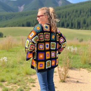 May include: A colorful, handmade crochet cardigan featuring a patchwork design. The cardigan showcases a variety of vibrant squares in shades of orange, yellow, blue, green, and purple, set against a black background. The garment is worn outdoors.