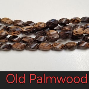 May include: A strand of brown and black wooden beads. The beads are oval shaped and have a textured surface. Old Palmwood.