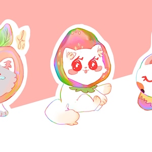 May include: Three white cats wearing fruit costumes. The first cat is wearing a pink and red apple costume. The second cat is wearing a red and green watermelon costume. The third cat is wearing a yellow banana costume.