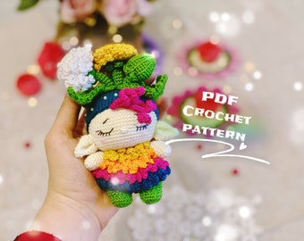 Puede incluir: Una muñeca amigurumi de crochet con una corona de flores, vestida con un vestido colorido y sosteniendo una flor. La muñeca está hecha con hilo de lana en tonos de verde, amarillo, naranja, rosa, azul y blanco. La muñeca está sentada en una mano, y el fondo está desenfocado.