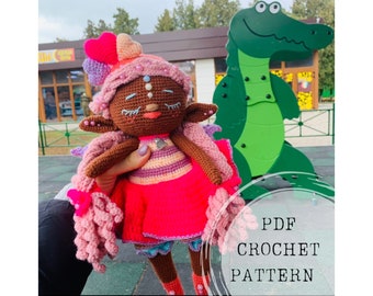 Puede incluir: Patrón de crochet PDF para una muñeca rosa y morada con piel morena, cabello rosa y un vestido rosa y morado. La muñeca sostiene un pequeño amuleto plateado. El texto "PDF CROCHET PATTERN" es visible en la imagen.