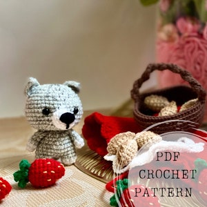 Puede incluir: Patrón de crochet PDF para un juguete amigurumi de lobo gris con fresas rojas y verdes, una cesta marrón con fresas de crochet marrón y una manta roja. El texto de la imagen dice "PDF CROCHET PATTERN".