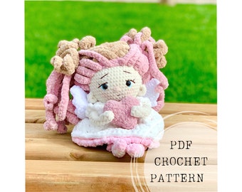 Puede incluir: Patrón de crochet PDF para una muñeca ángel rosa y blanca que sostiene un corazón rosa. La muñeca tiene el pelo de lana marrón y rosa y alas blancas.