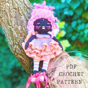 Puede incluir: Patr&oacute;n de crochet PDF para una mu&ntilde;eca rosa y negra con una corona rosa y una falda con volantes. La mu&ntilde;eca est&aacute; sentada en una rama de &aacute;rbol.