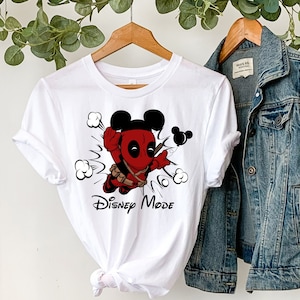 May include: White t-shirt with a cartoon image of Deadpool dressed as Mickey Mouse. The shirt has the text "Disney Mode" printed on it.
