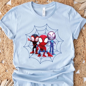 May include: Light blue t-shirt with a graphic of three cartoon Spider-Man characters in a web. The characters are red, black, and white.