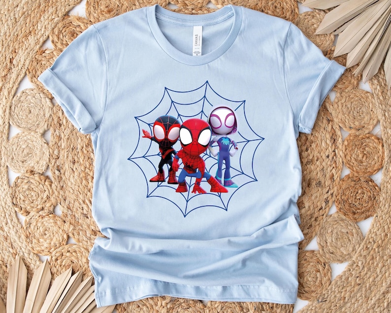 May include: Light blue t-shirt with a graphic of three cartoon Spider-Man characters in a web. The characters are red, black, and white.