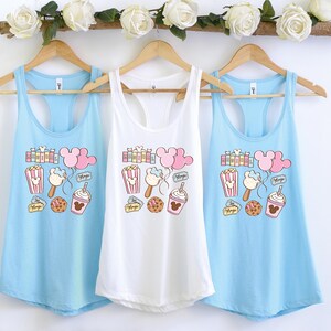 Pu&ograve; includere: Tre canottiere di colore azzurro chiaro, bianco e azzurro chiaro. Ogni canottiera presenta una stampa grafica di orecchie di Topolino, popcorn, un gelato di Topolino, un pretzel di Topolino e una tazza di Topolino. Il testo "Magic" &egrave; stampato su ogni canottiera.